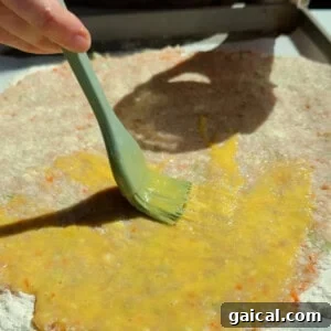 Buffalo Chicken Protein Bars — Crispy Baked Savory Snack 13 Brushing egg wash over chicken protein bar mixture on a floured parchment-lined surface
