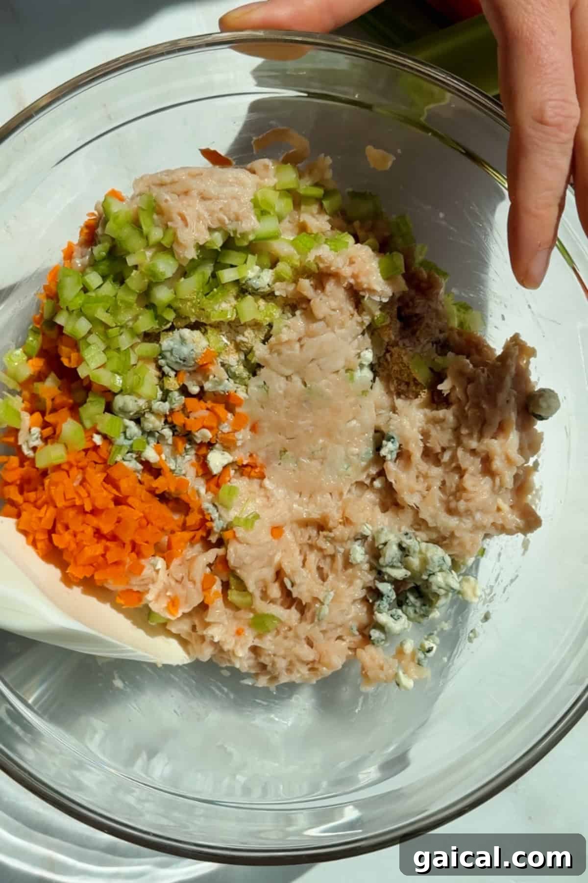 Buffalo Chicken Protein Bars — Crispy Baked Savory Snack 4 Mixing ground chicken, carrots, celery, blue cheese crumbles, and seasonings in a glass bowl for protein bars