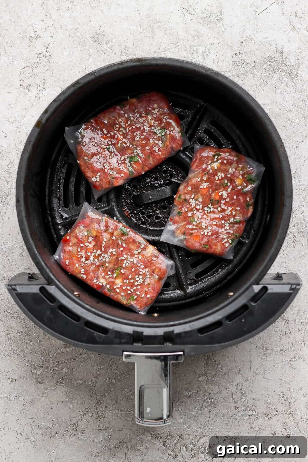 Three uncooked frozen salmon filets coated with marinade and sesame seeds arranged in the basket of an air fryer.
