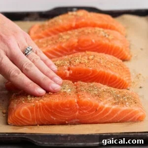 Rubbing seasoning onto raw salmon fillets on a parchment-lined baking sheet.