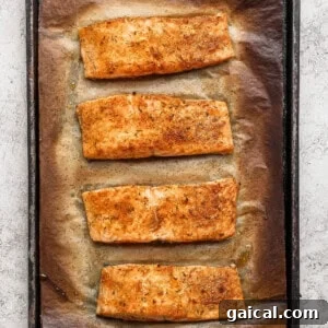 Four golden broiled salmon fillets on a parchment-lined baking sheet fresh from the oven.