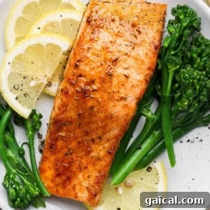 Broiled salmon fillet served on a white plate with lemon slices and steamed broccolini.