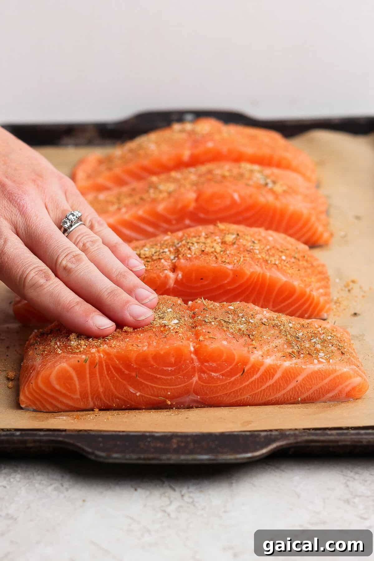 Rubbing seasoning onto raw salmon fillets on a parchment-lined baking sheet.