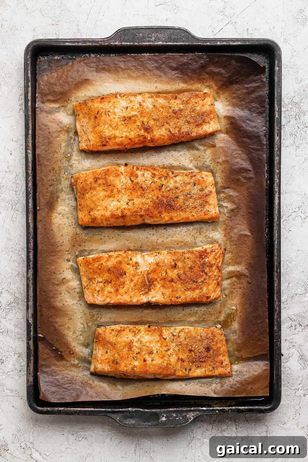 Four golden broiled salmon fillets on a parchment-lined baking sheet fresh from the oven.