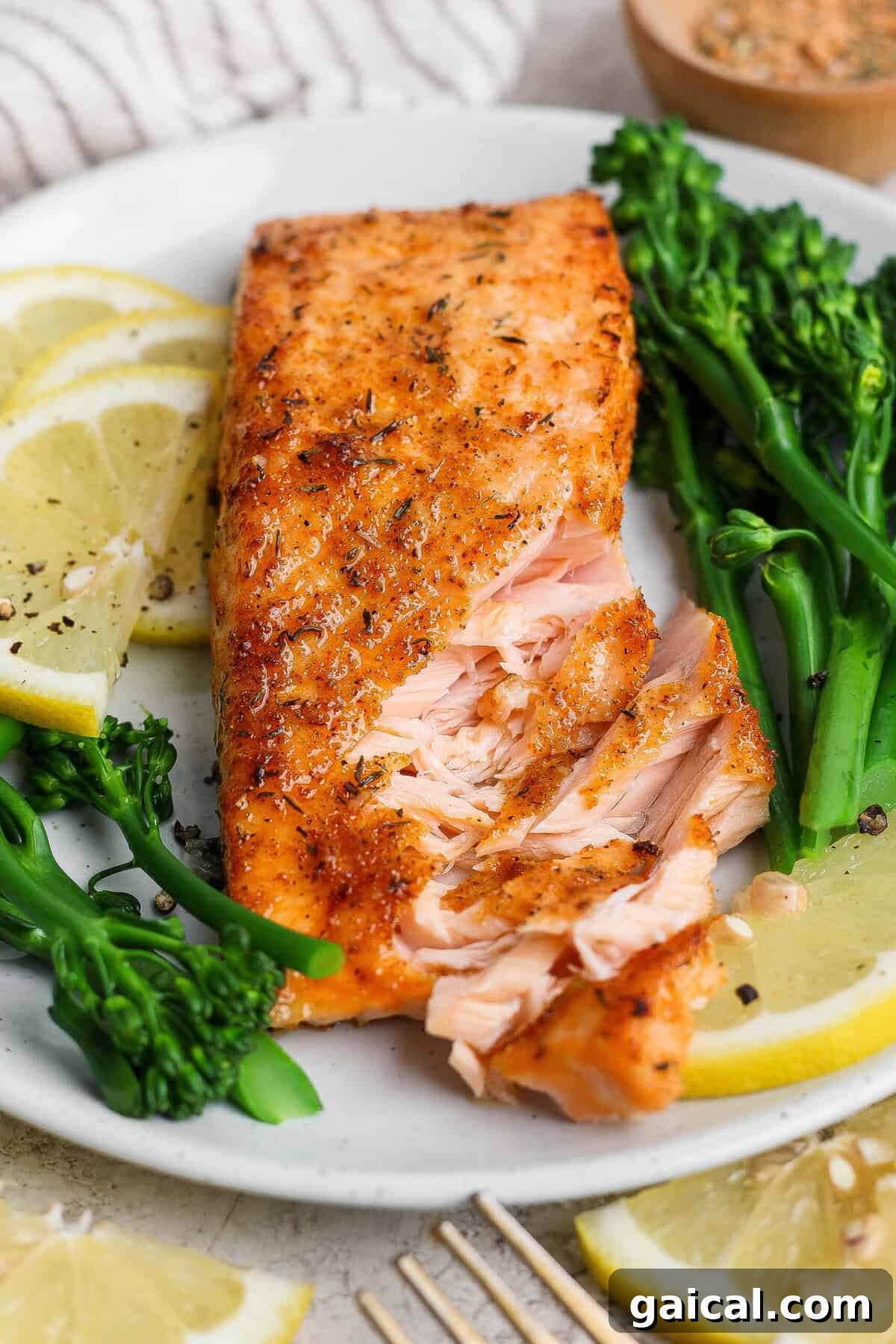 Flaky broiled salmon fillet on a white plate with broccolini and lemon, showing the tender interior.