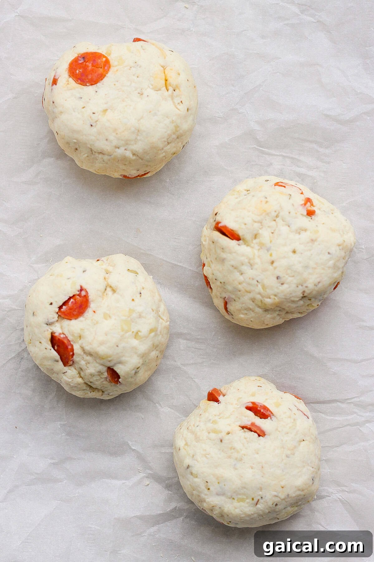 Four pizza protein bagel dough balls with pepperoni on parchment paper