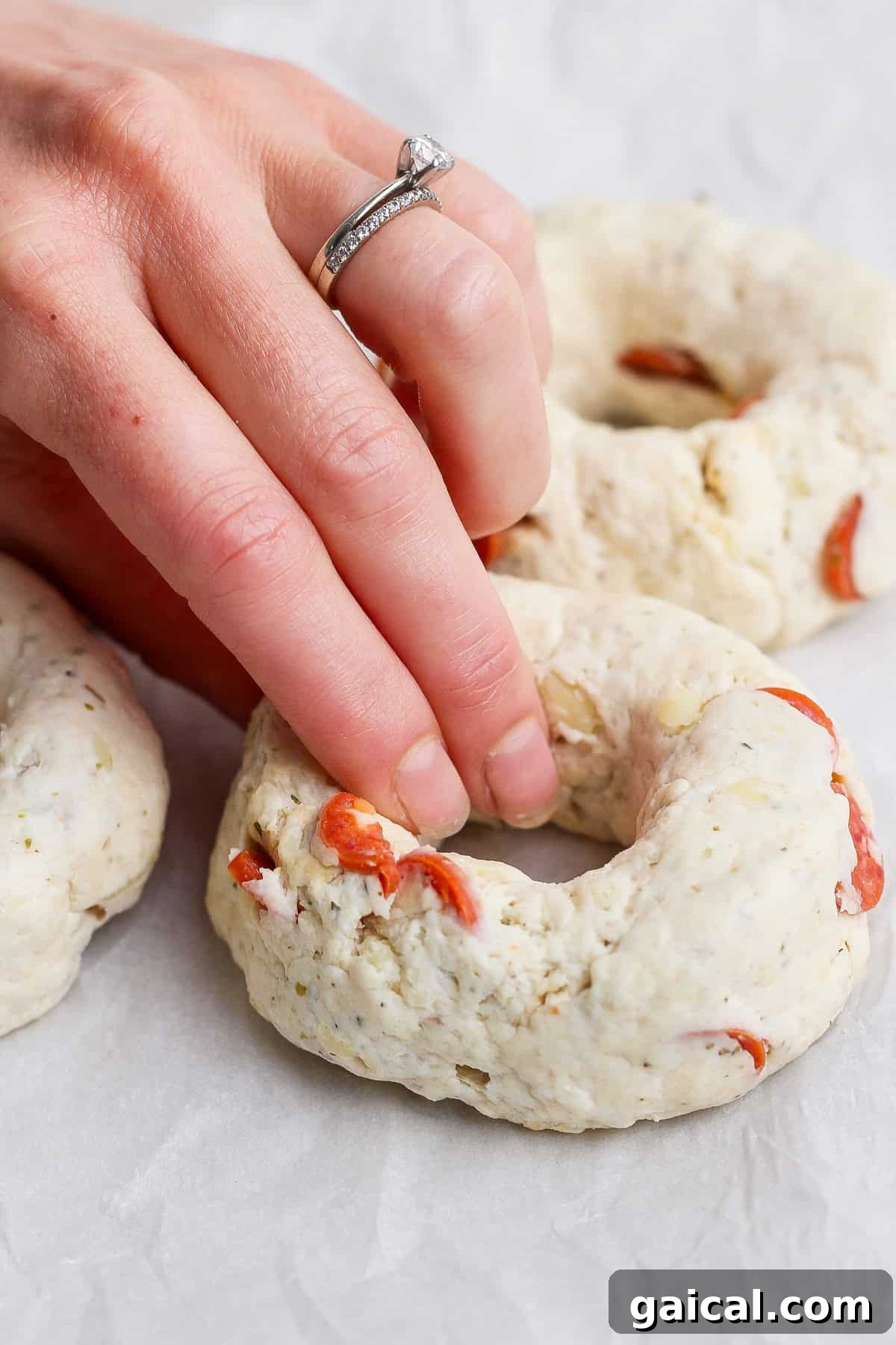 Hand shaping pizza protein bagel dough with pepperoni pieces on parchment paper