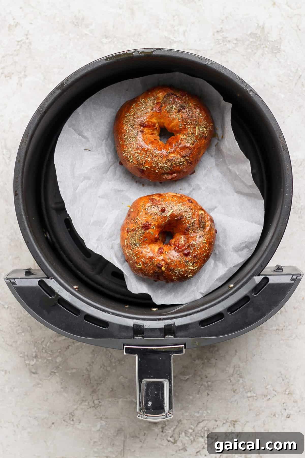 Two baked pizza protein bagels with Italian seasoning in an air fryer basket