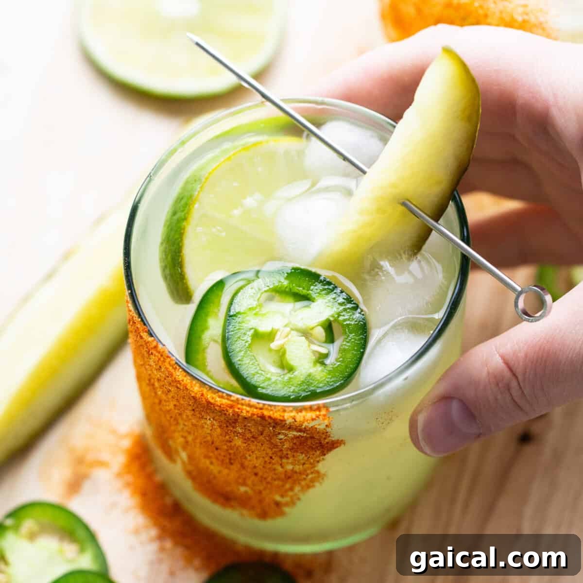 A hand holding a glass of drink with a pickle and lime.