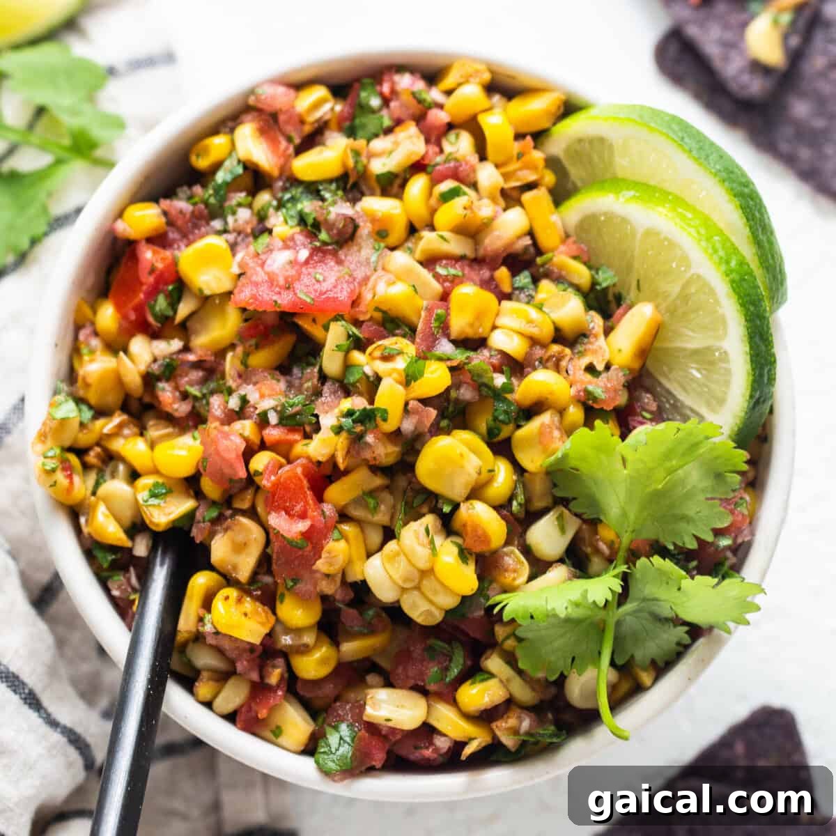 mexican corn salad in a white bowl with limes and tortilla chips.