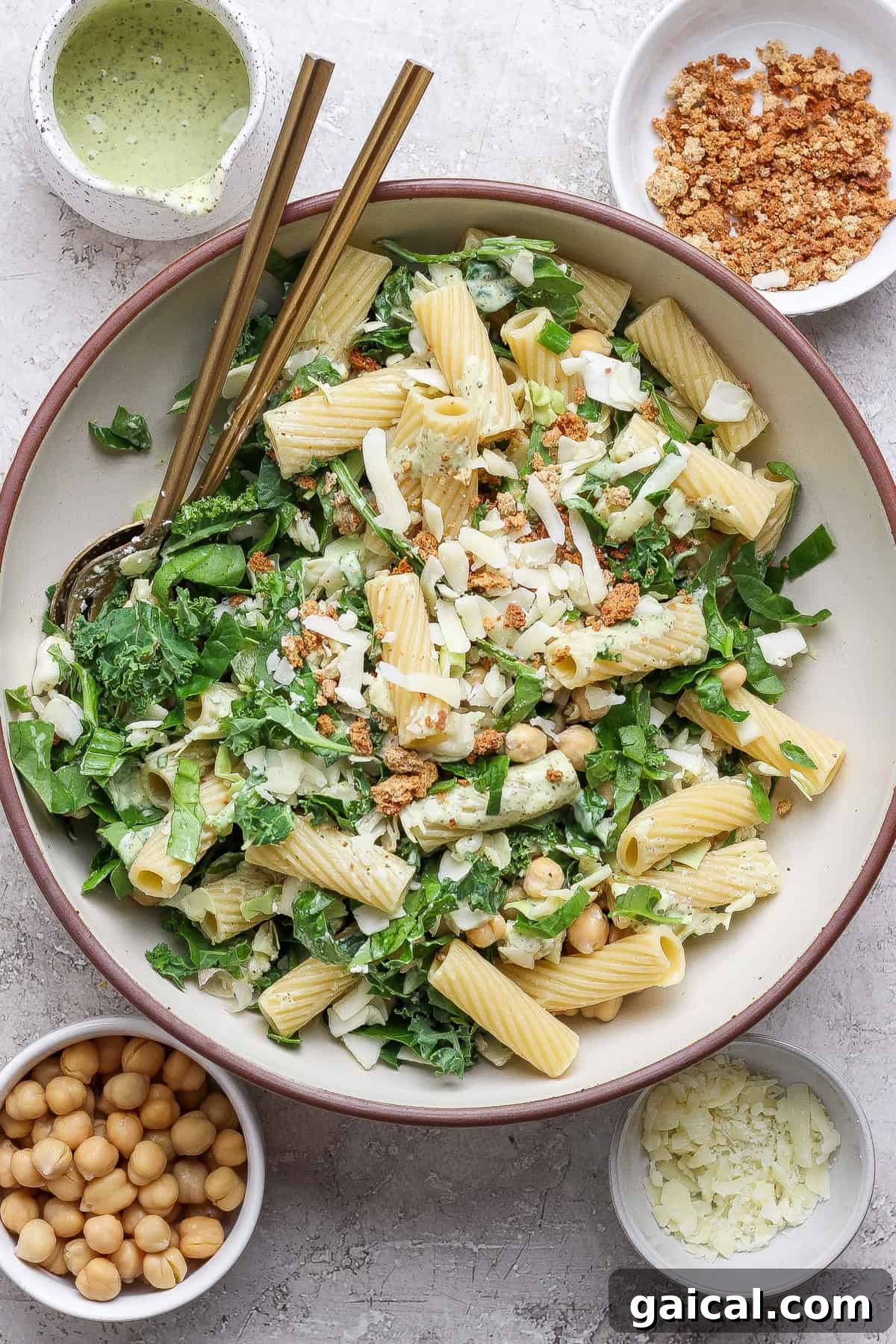 A bowl of pasta salad with greens, chickpeas, cheese, and crumb topping, surrounded by small bowls of chickpeas, cheese, crumbs, and dressing.