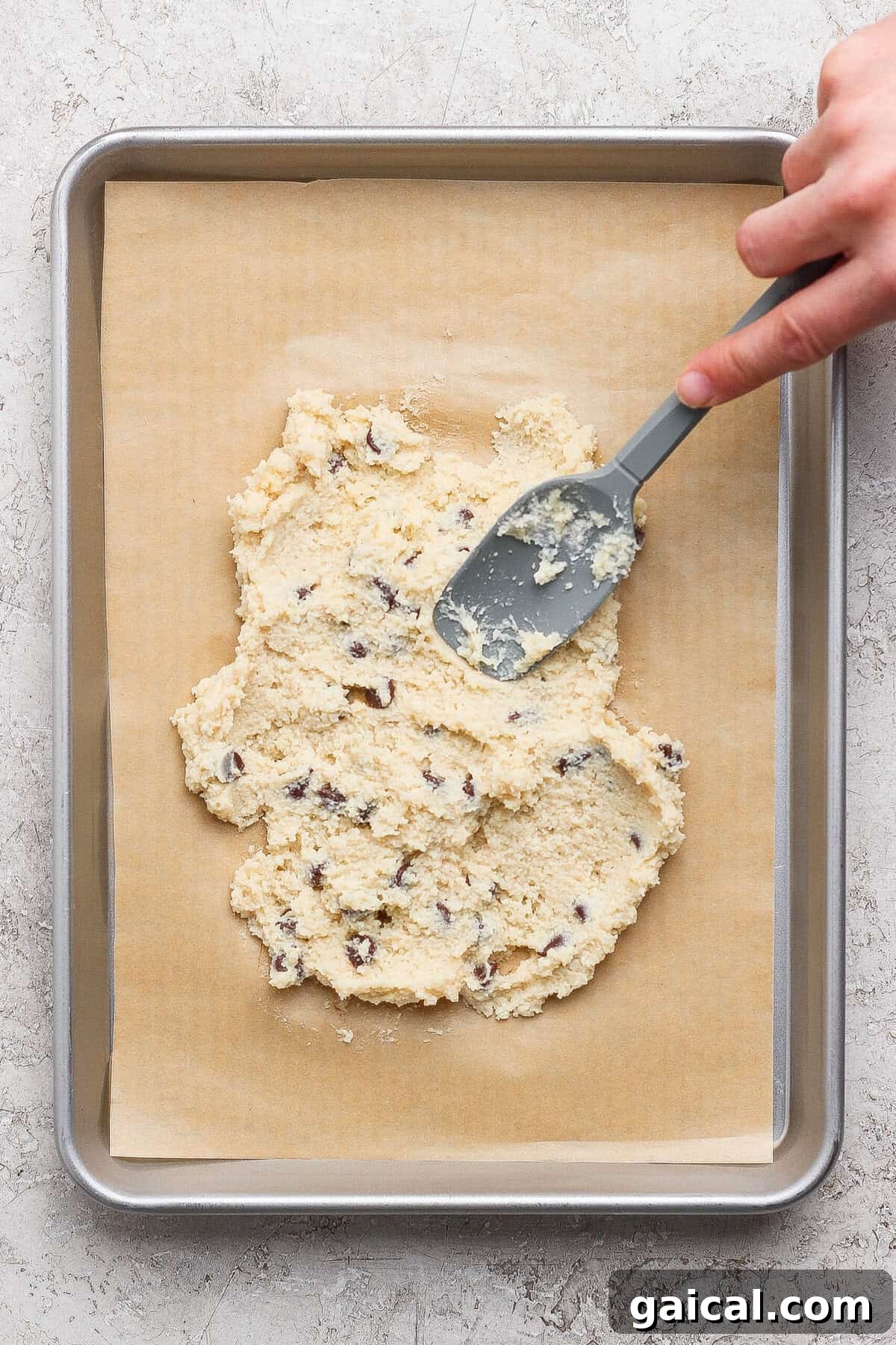 spreading cottage cheese cookie dough onto a parchment-lined baking sheet