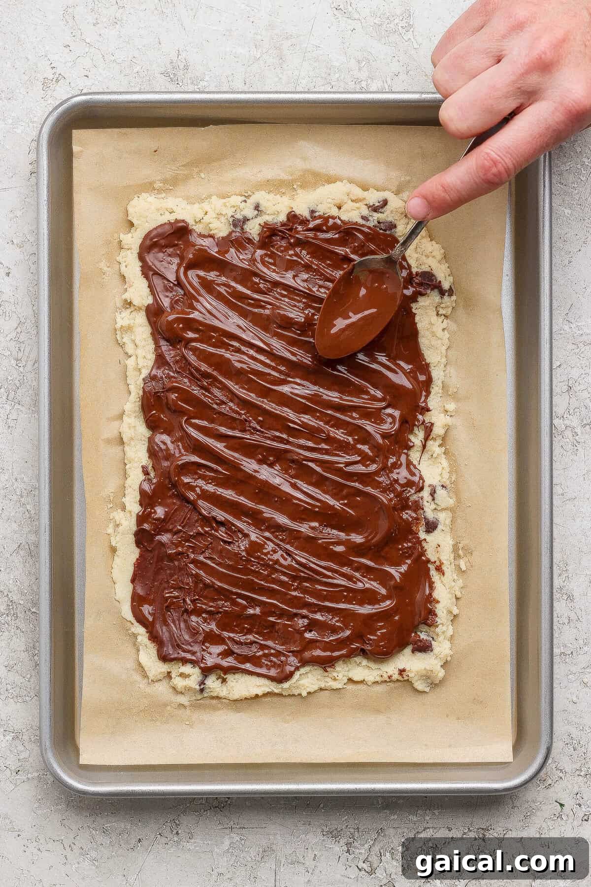 spreading melted chocolate over cottage cheese cookie dough bark with a spoon