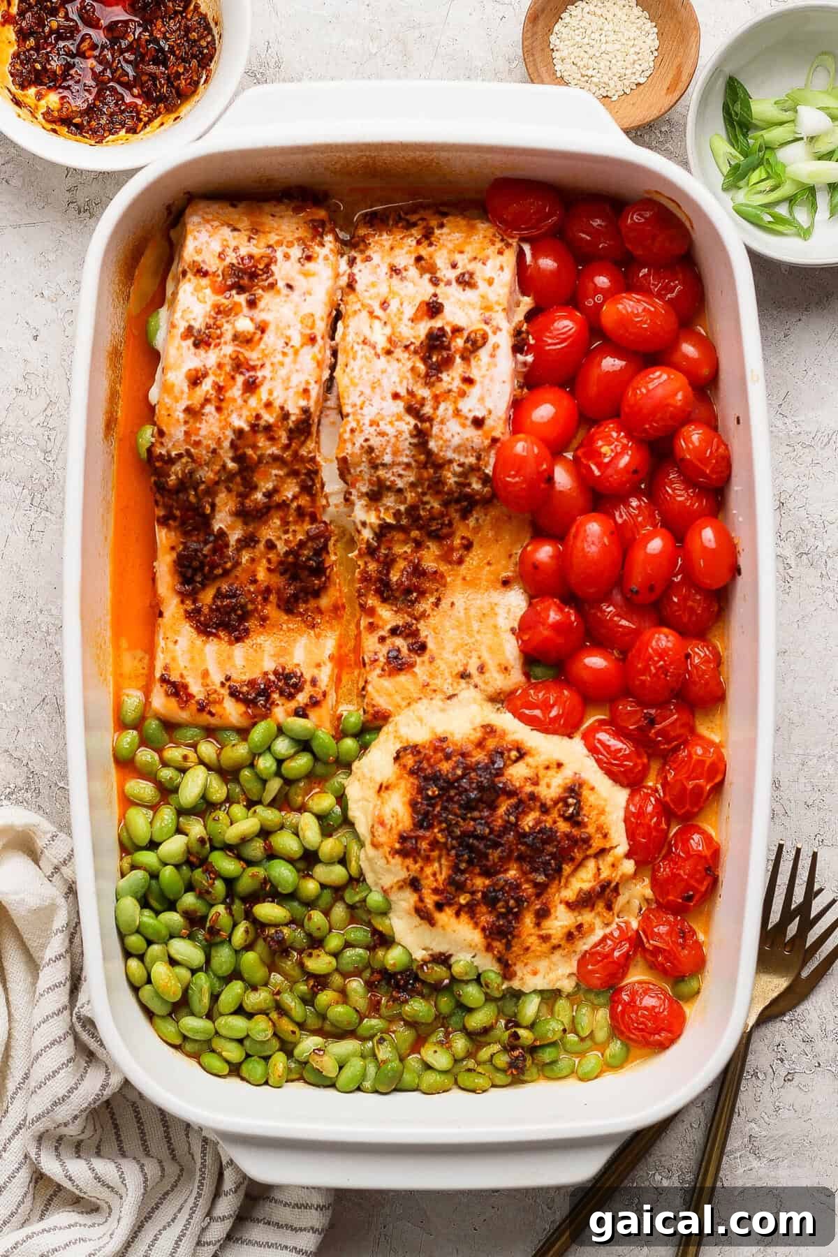 Close-up of baked chili crunch salmon with burst cherry tomatoes and edamame in a casserole dish