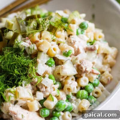 A bowl of pasta salad with peas, diced pickles, chunks of chicken, and fresh dill on top.