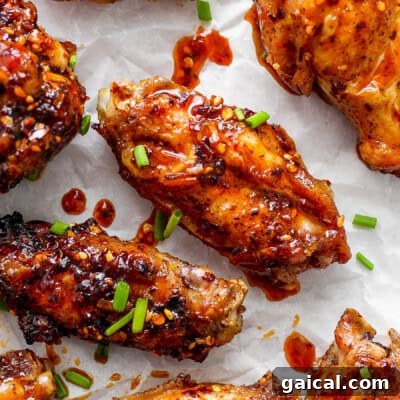 Glazed chicken wings on parchment paper garnished with sesame seeds and chopped green onions.