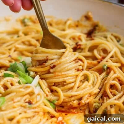A close-up of a fork twirling spaghetti noodles coated in a creamy orange sauce, garnished with sliced green onions.