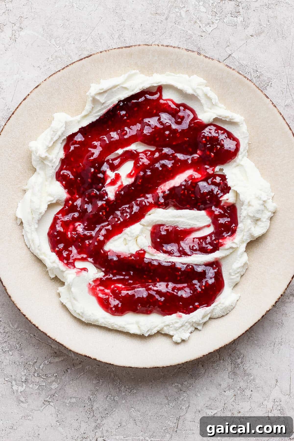 raspberry jam swirled over spread goat cheese on a plate