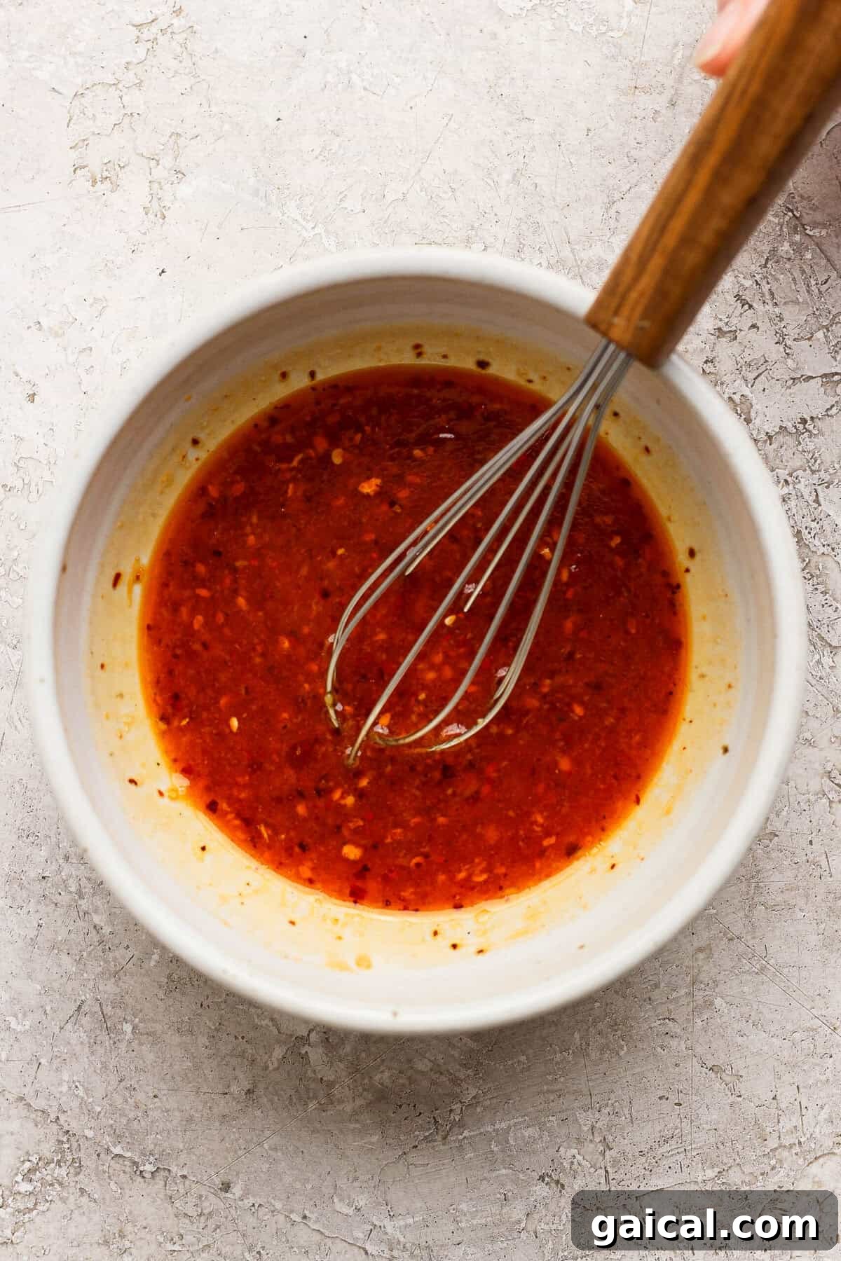 whisking chili crunch dressing with sesame oil ginger and lime in a ceramic bowl