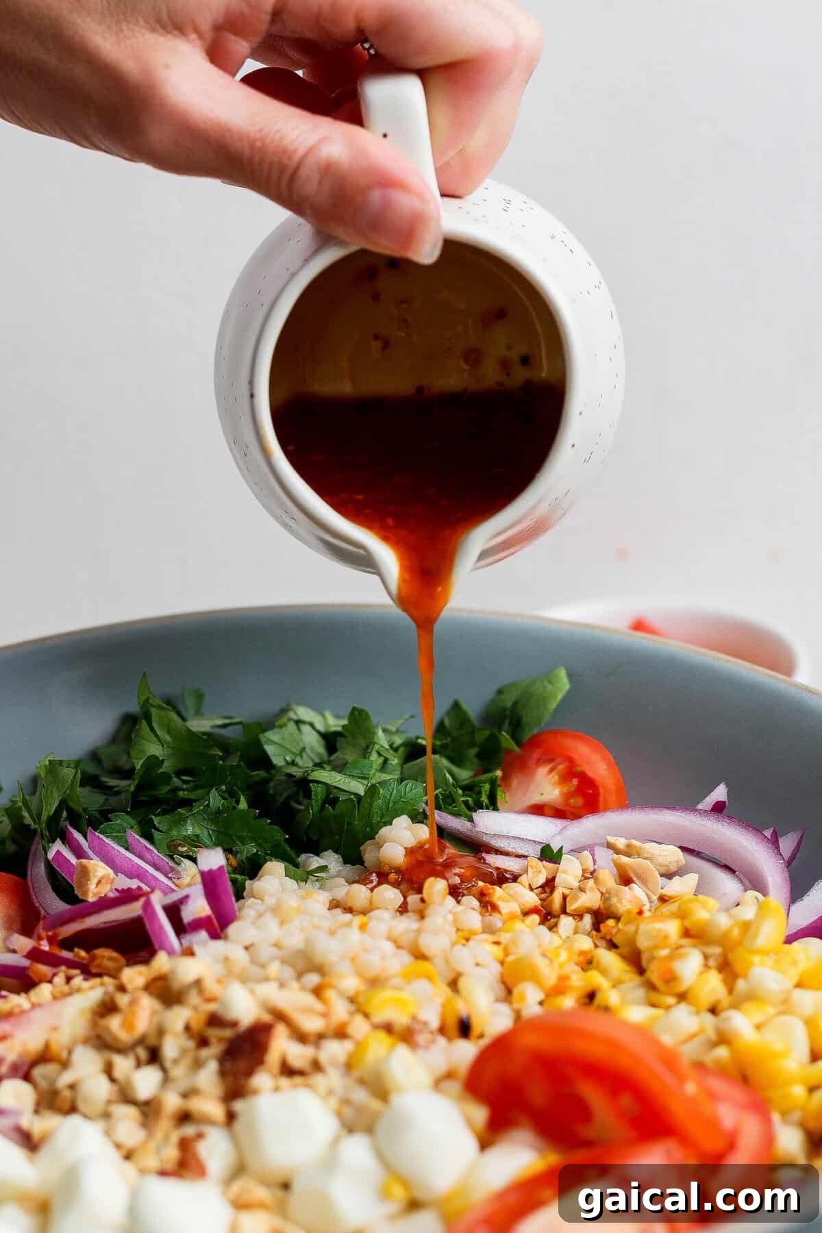 pouring chili crunch dressing over corn tomato salad from a pitcher