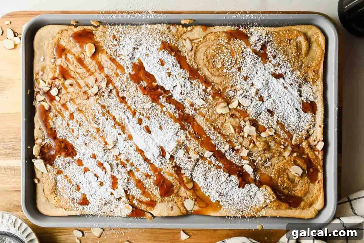 Baked sheet pan almond croissant pancakes dusted with powdered sugar and drizzled with maple syrup.