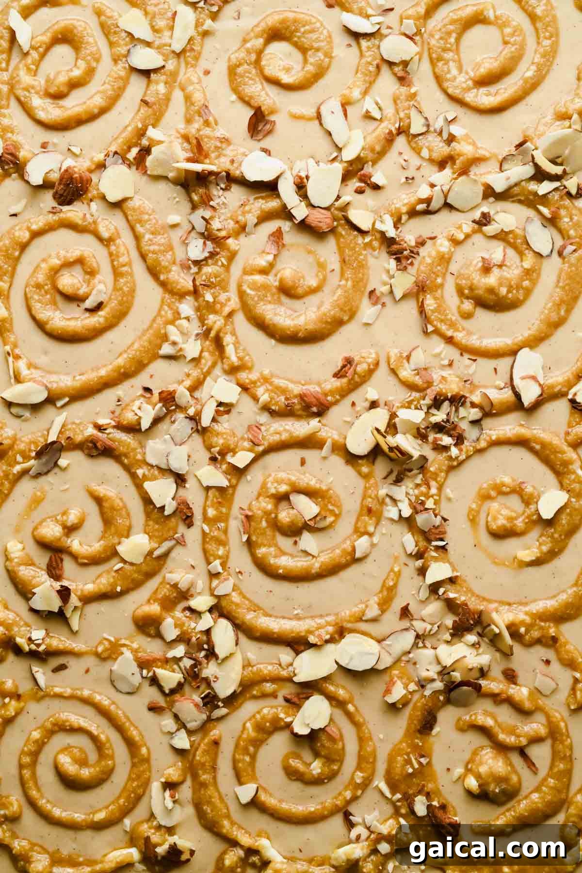 Sheet pan pancake batter topped with piped frangipane swirls and sliced almonds before baking.