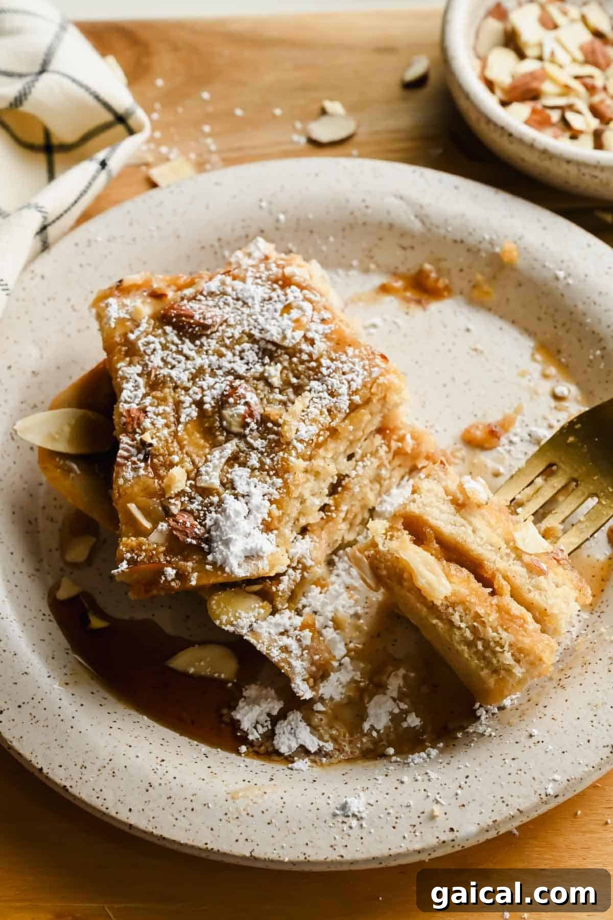 Stacked sheet pan almond croissant pancakes on a plate with maple syrup and powdered sugar.