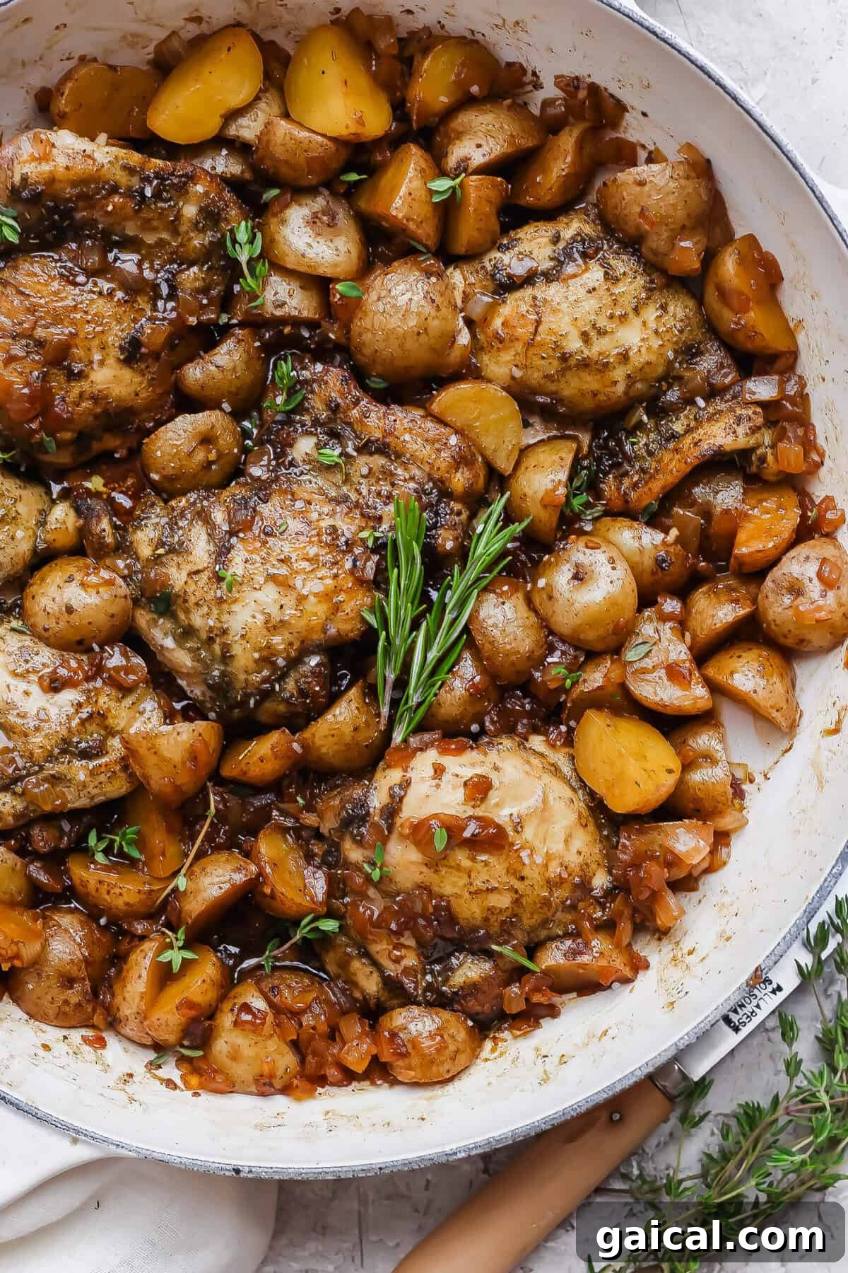 Apple cider chicken thighs nestled with baby potatoes and onion in a glossy skillet sauce.