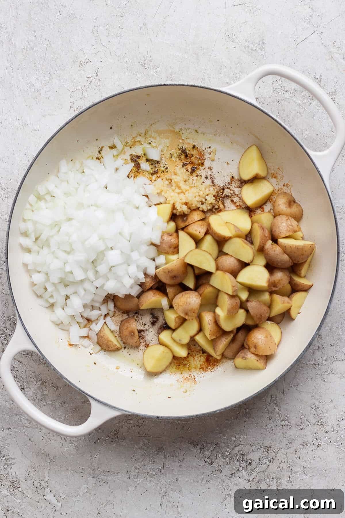 Diced white onion, minced garlic, and quartered baby potatoes in a white skillet.