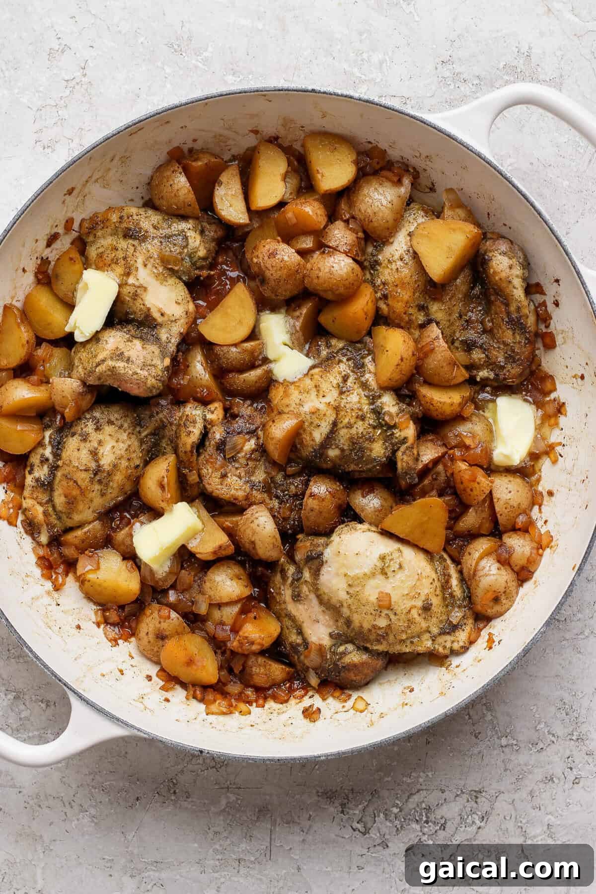 Butter melting into the apple cider pan sauce around chicken thighs, potatoes, and onion.