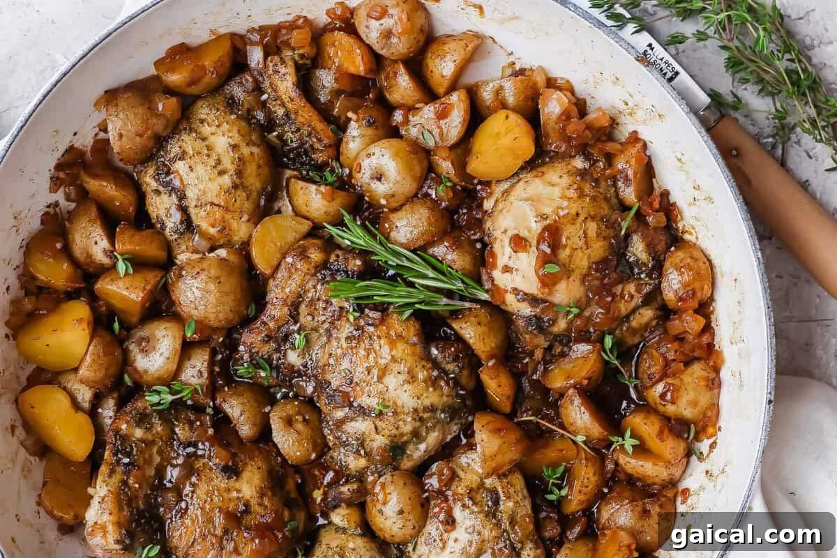 Apple cider chicken thighs nestled with baby potatoes and onion in a glossy skillet sauce.