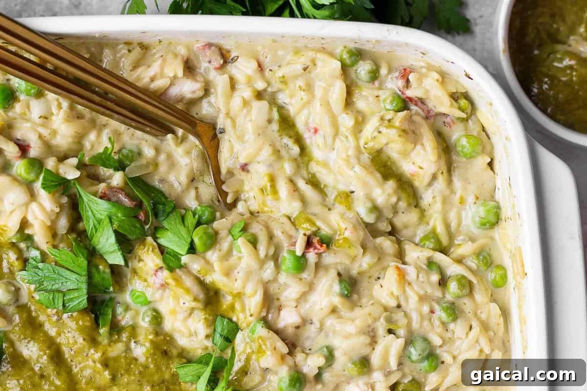 Close-up of creamy chicken pesto orzo with peas, sun-dried tomatoes, pesto, and fresh parsley.