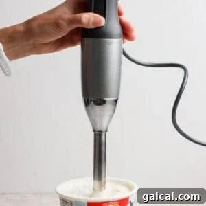 An immersion blender blending cottage cheese dip directly in the cottage cheese container.