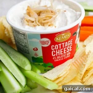 Finished cottage cheese French onion dip topped with golden onions and served in the cottage cheese container with potato chips and celery.