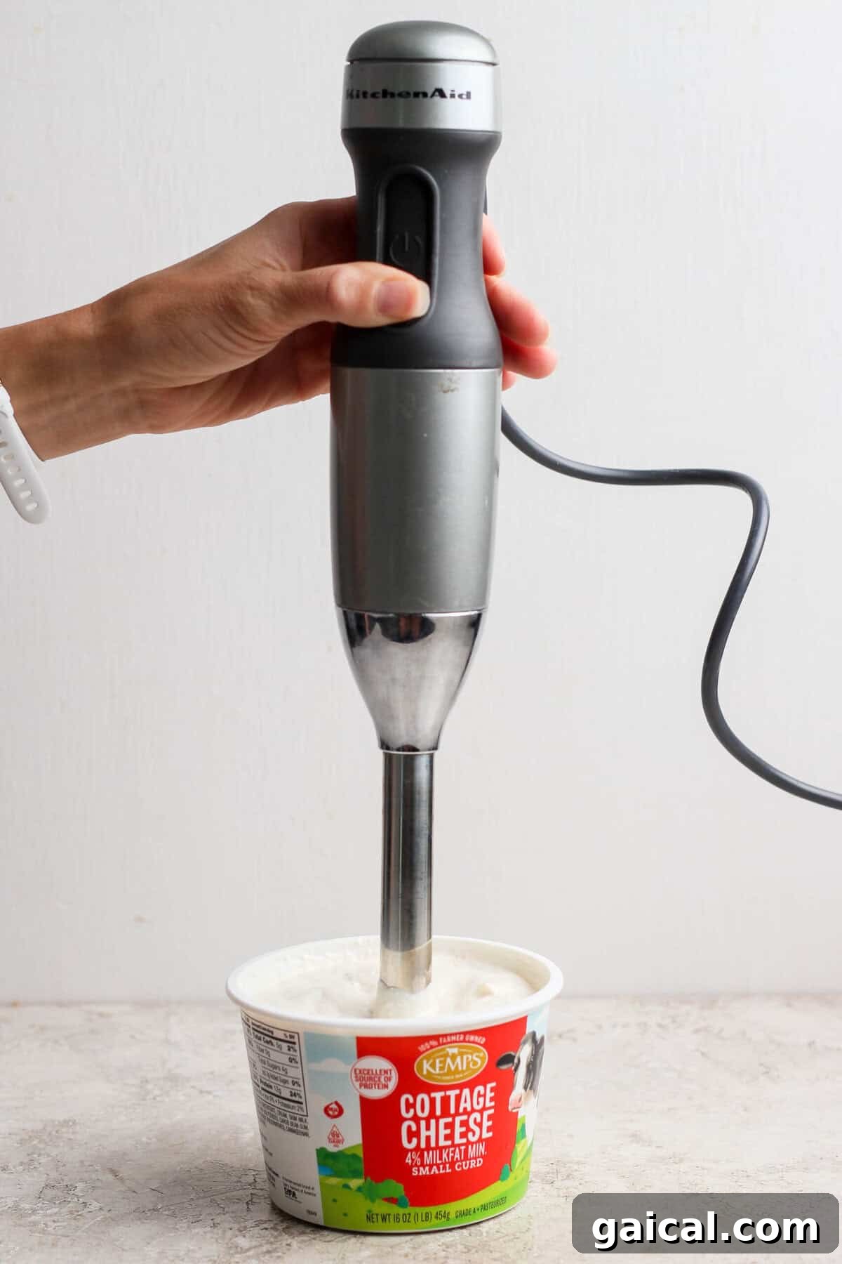 An immersion blender blending cottage cheese dip directly in the cottage cheese container.