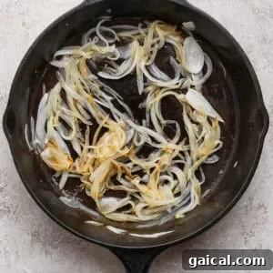Soft golden sliced onions in a cast-iron skillet for cottage cheese French onion dip.