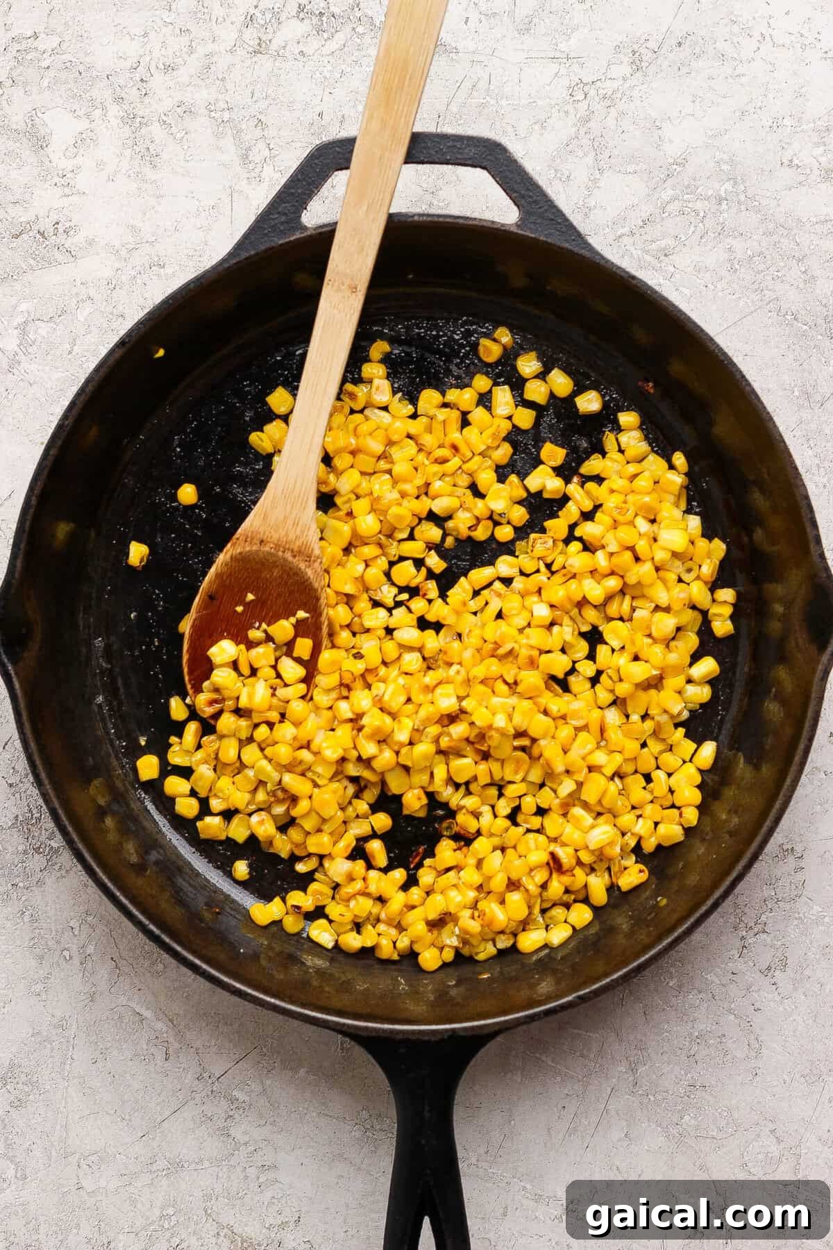 Sweet corn kernels browning in avocado oil in a cast-iron skillet.