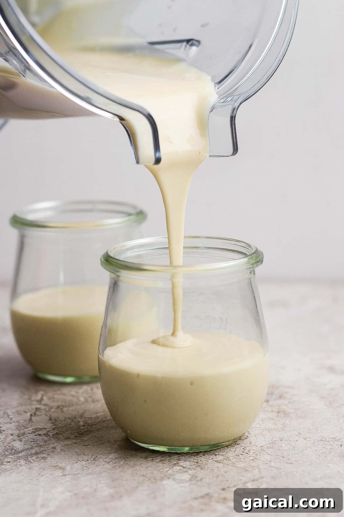 Blended cottage cheese cheesecake mixture being poured into individual clear dessert jars.
