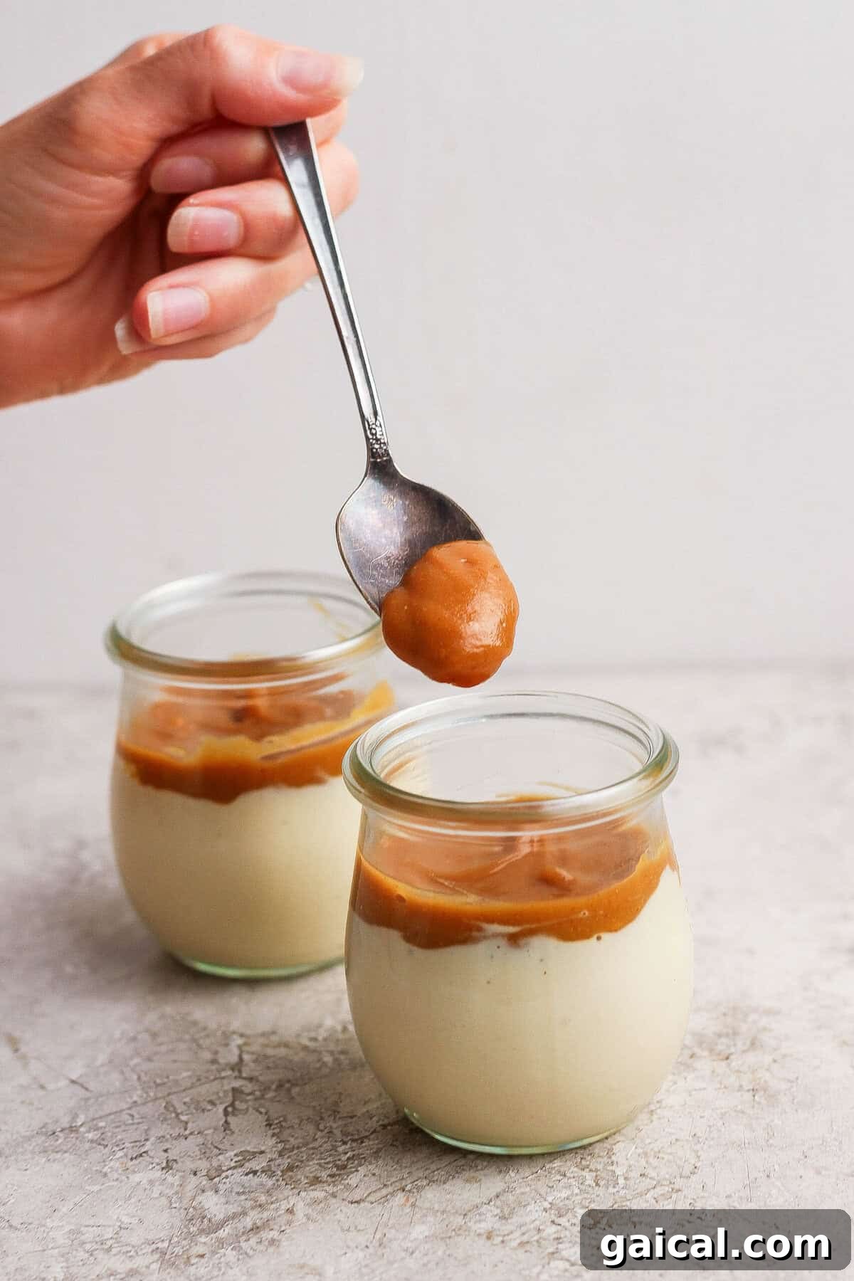 Maple peanut butter being spooned over the cottage cheese layer in individual dessert jars.