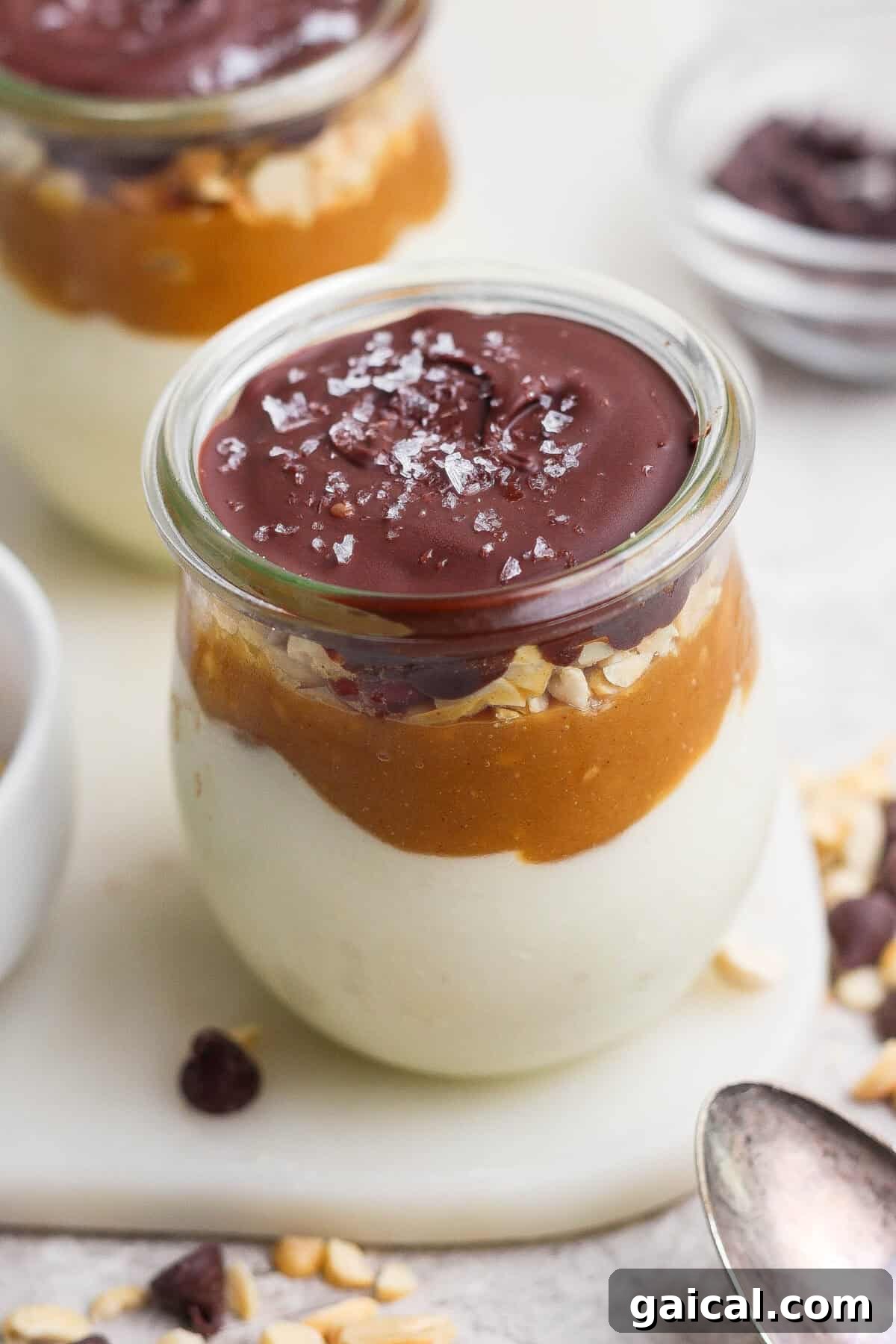 Individual Snickers cheesecake cup layered with blended cottage cheese, maple peanut butter, salted peanuts, and a glossy chocolate shell.